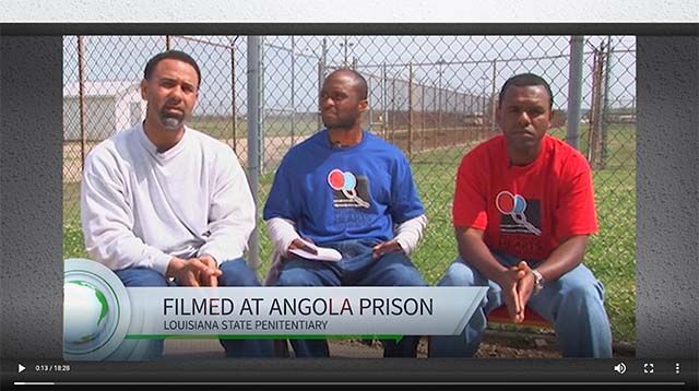 Three people sit in front of a chain-link fence at Angola Prison, Louisiana State Penitentiary.