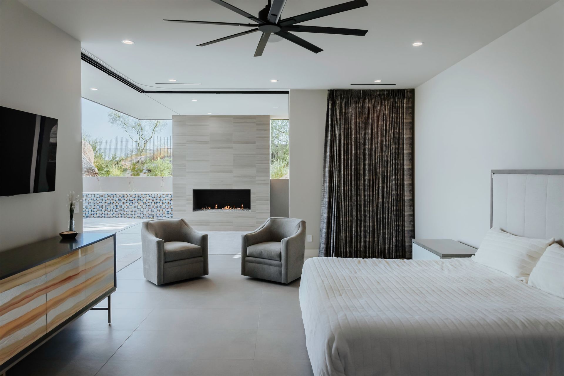 A bedroom with a bed , two chairs and a fireplace.