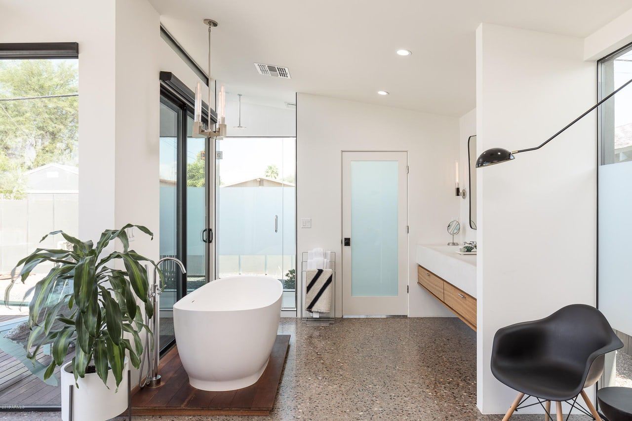 A bathroom with a tub , sink , chair and plant.
