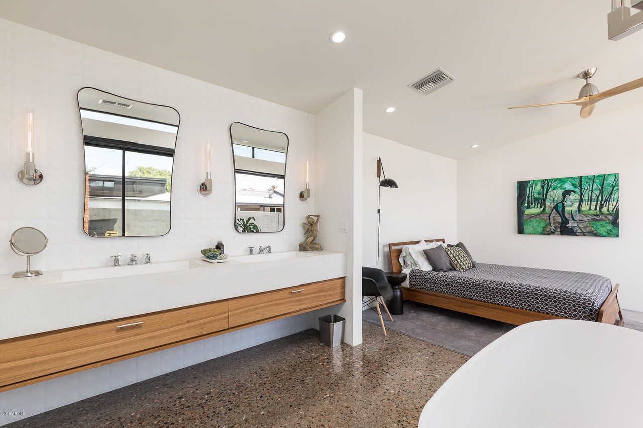 A bathroom with two sinks , two mirrors and a bed.