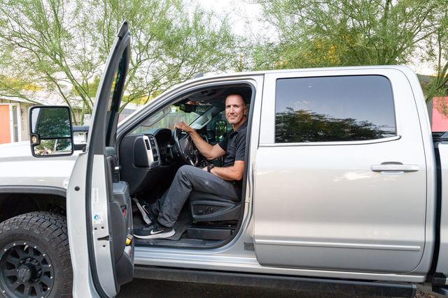 A man is sitting in the driver 's seat of a silver truck.