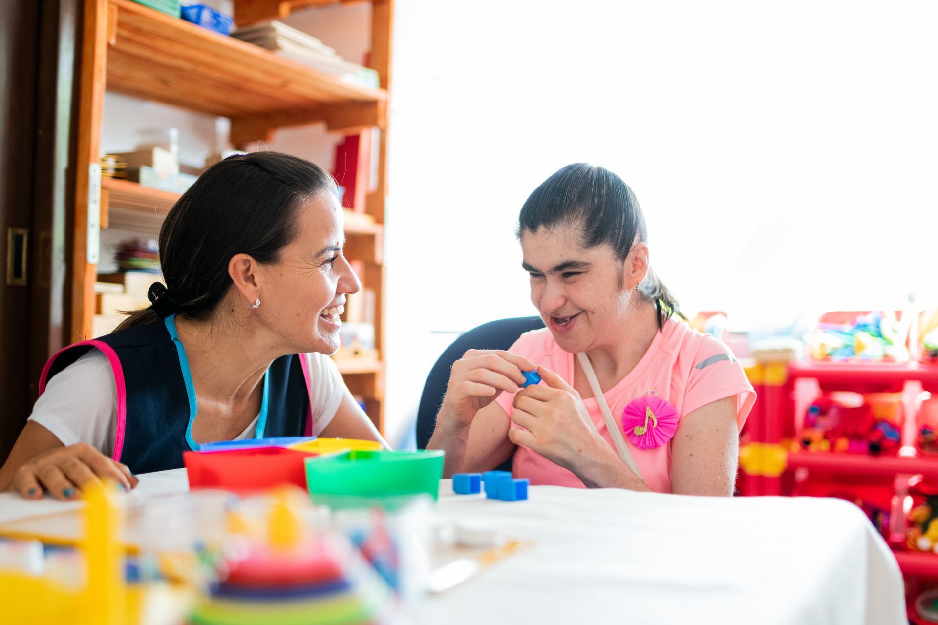 Woman assisting another woman working with blue blocks at a table.