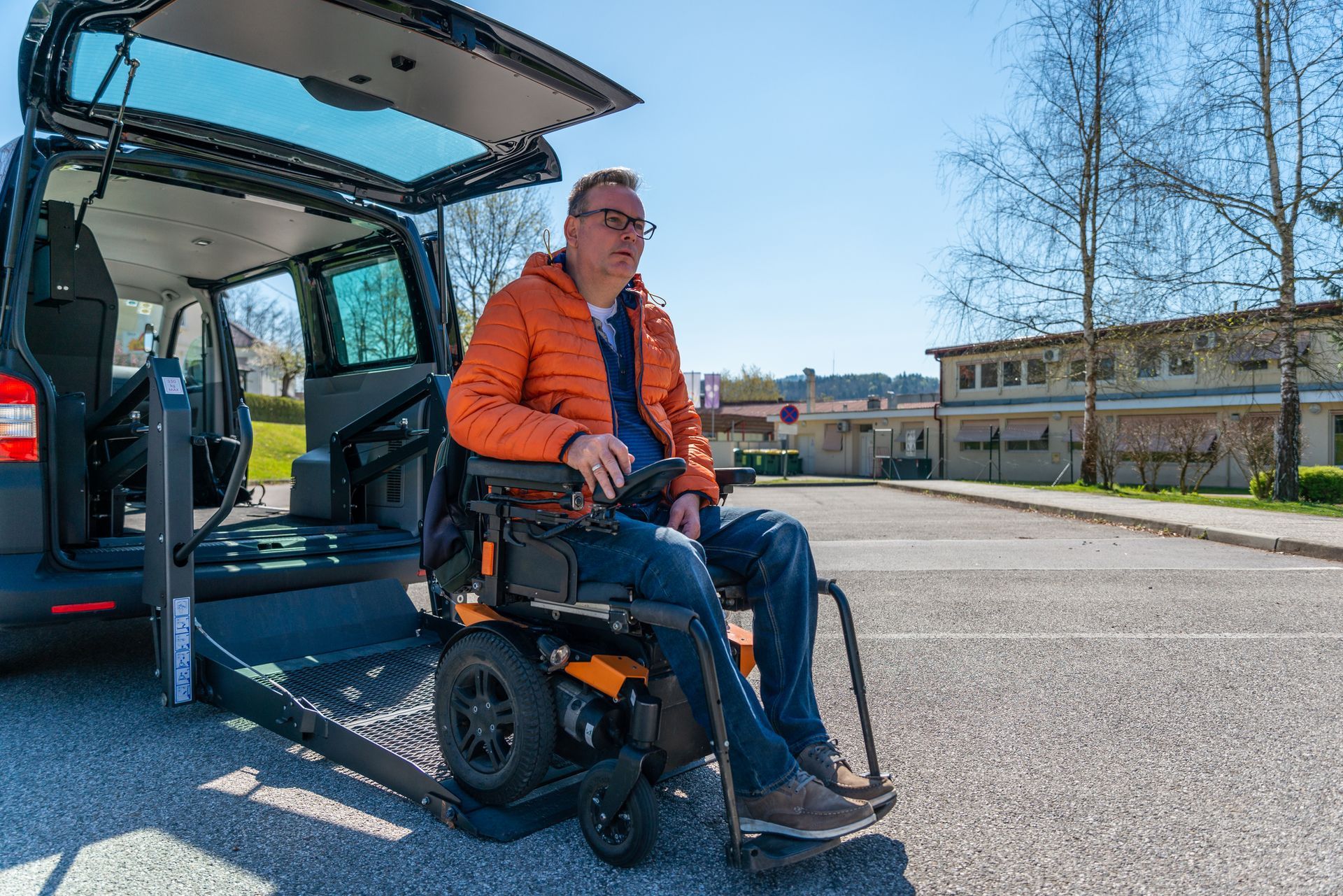 Man in wheelchair exiting accessible van via lift ramp outdoors. Sunny day.