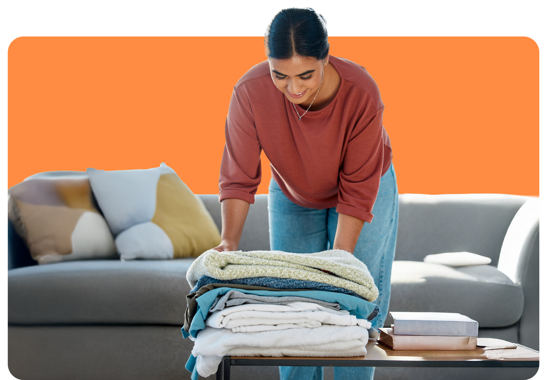 Woman folding laundry on a table in a living room, smiling.