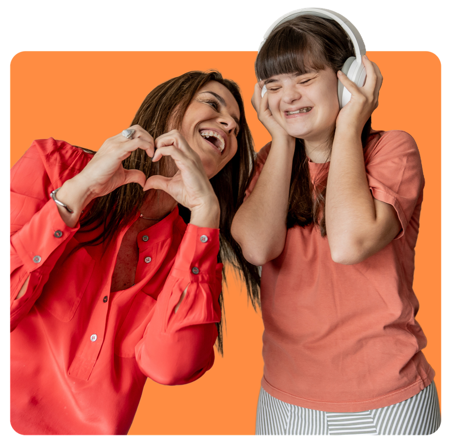 Woman forming a heart with hands, smiling at a person with Down syndrome wearing headphones and smiling.