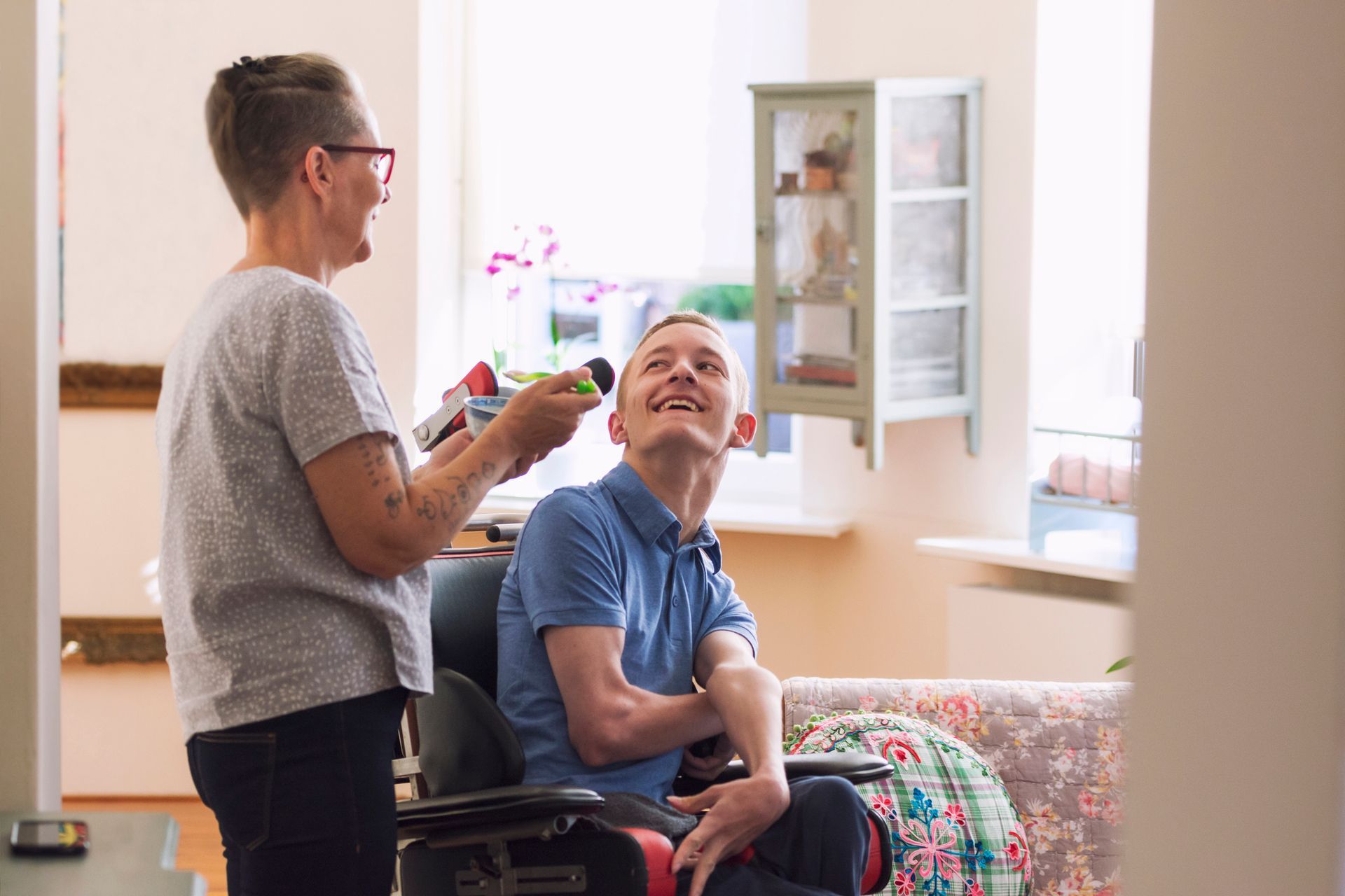 Woman holding toy for smiling person in wheelchair. Bright room, natural light.
