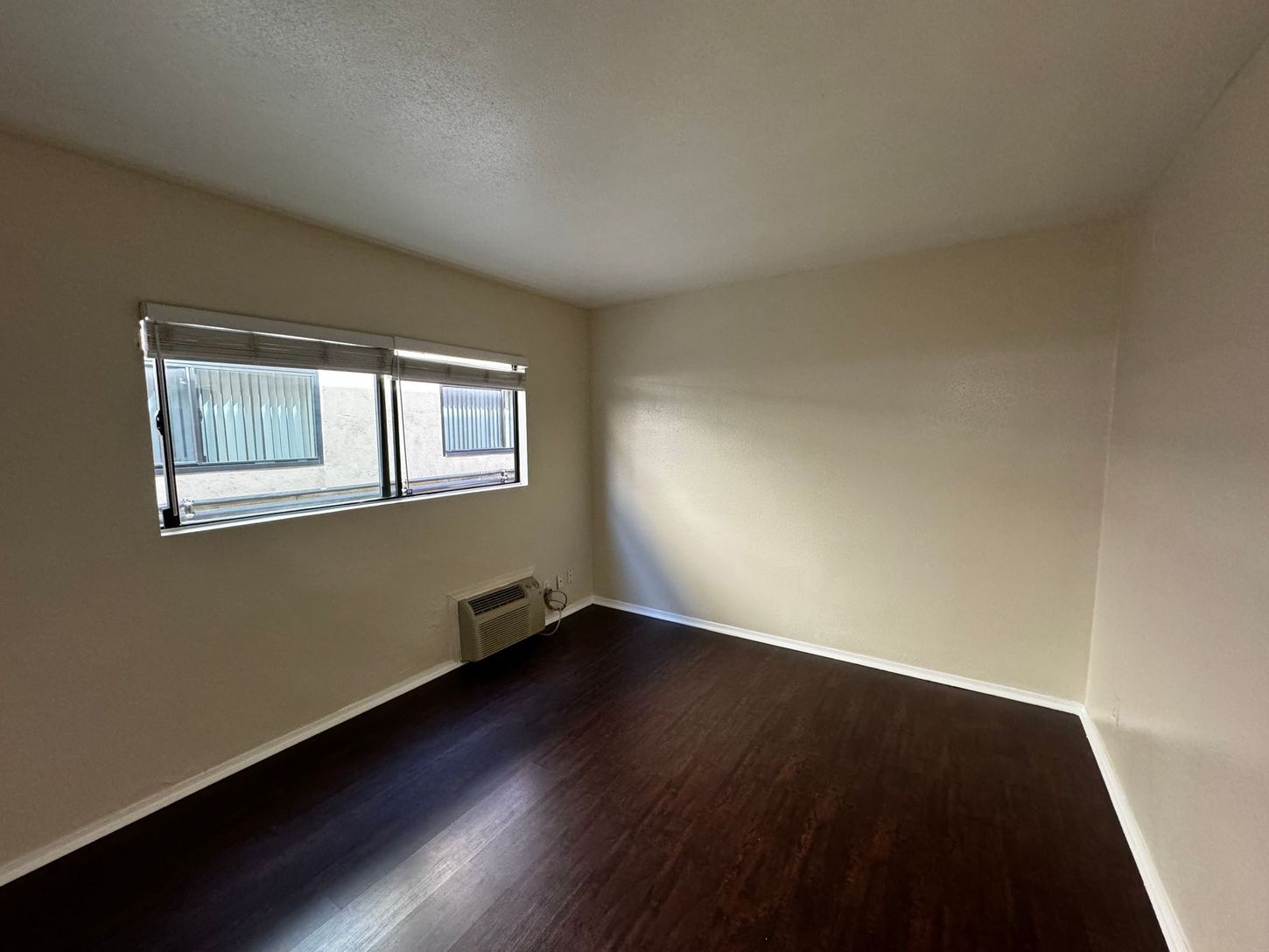 An empty room with hardwood floors and two windows.