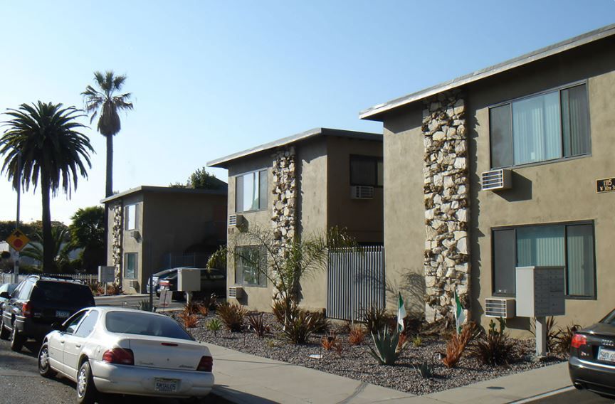 A row of apartment buildings with cars parked in front of them