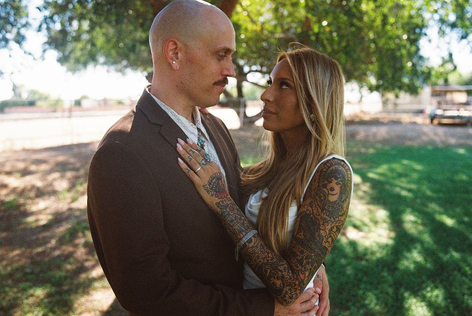A couple embracing outdoors in a sunlit park, gazing at each other.