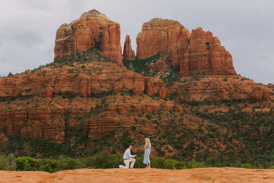 Two people proposing in front of red rock buttes under an overcast sky