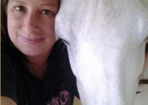 A woman is standing next to a white horse.