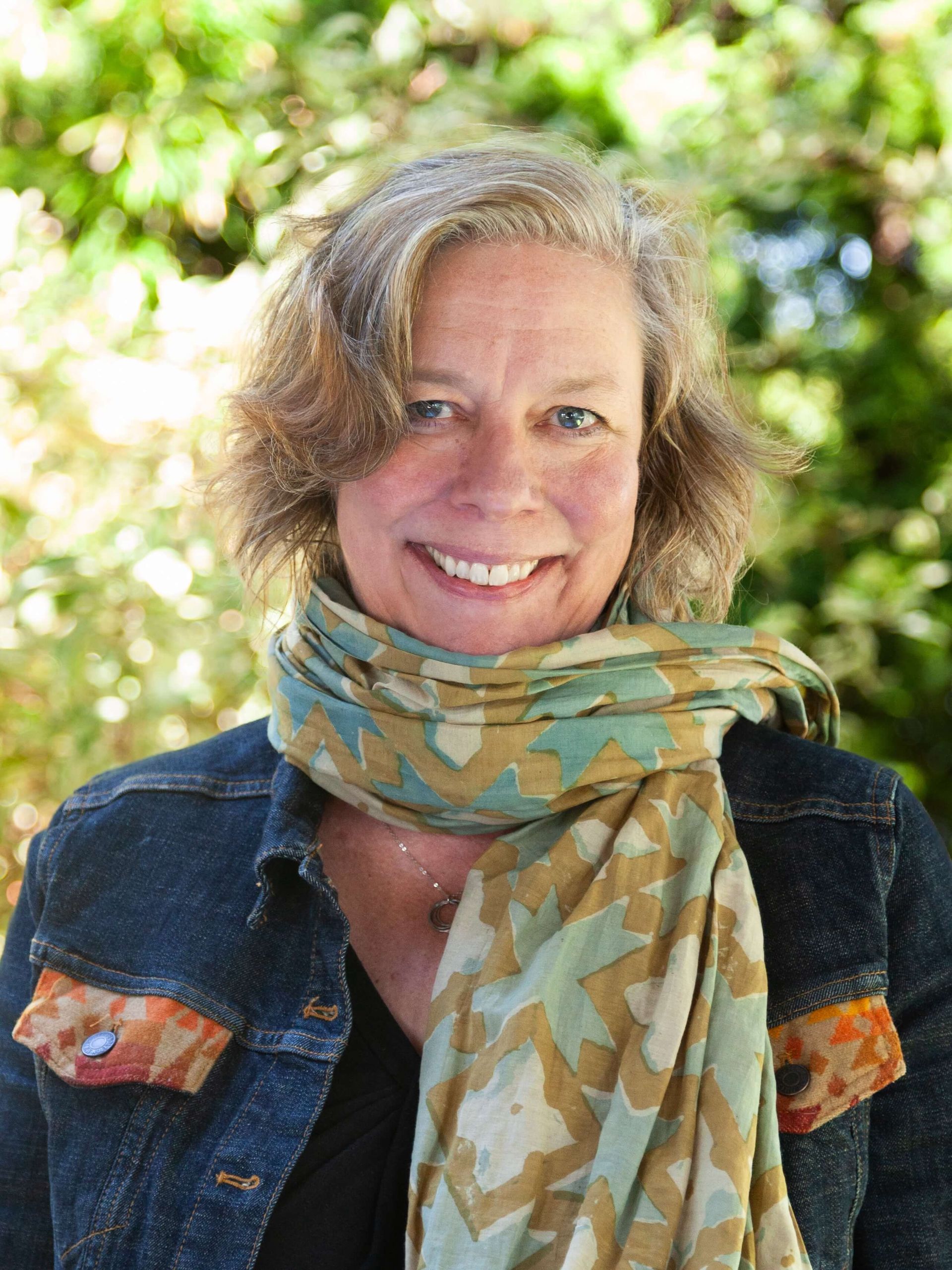 Woman with short hair smiling and wearing a scarf.