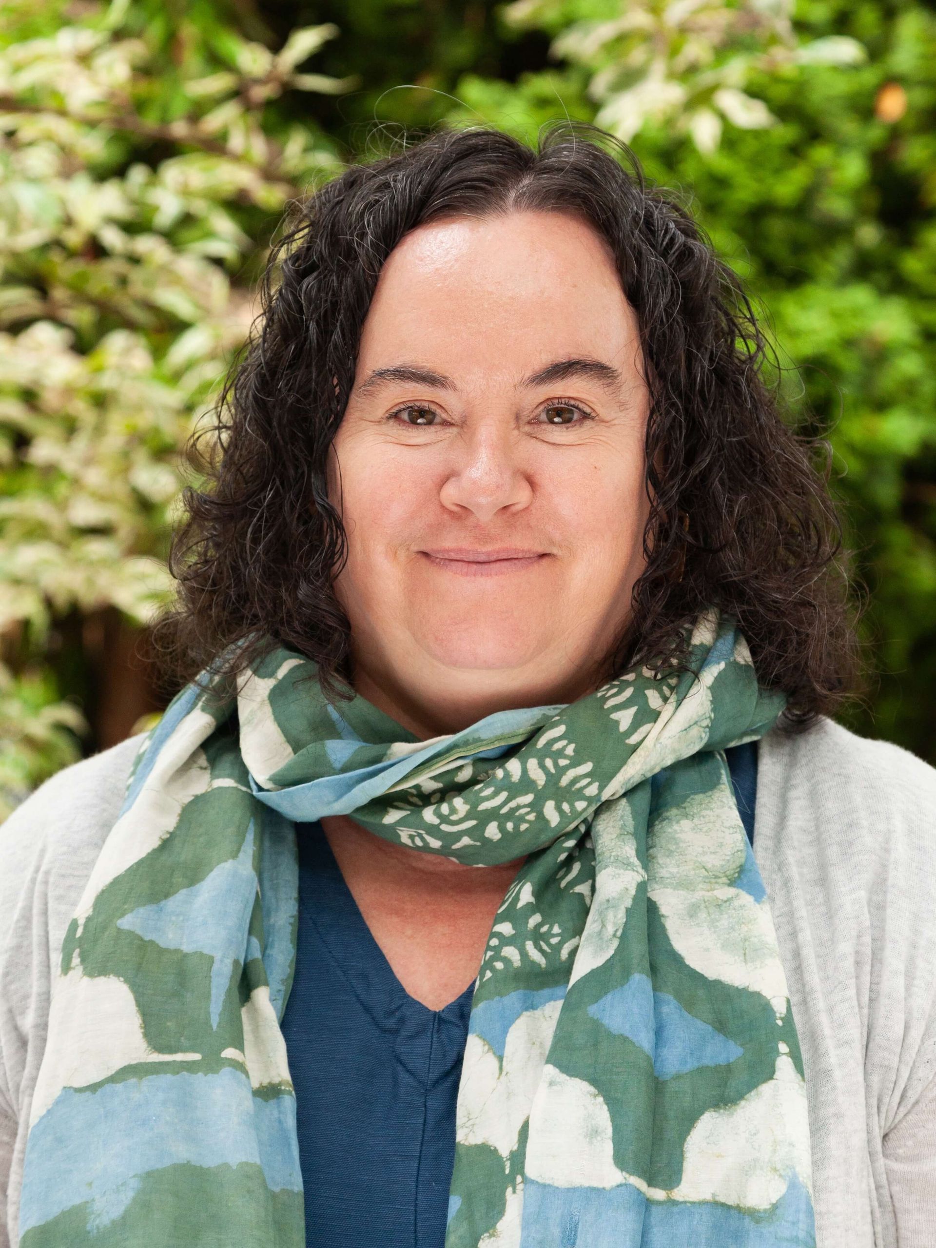 Woman with short curly brown hair wearing a scarf.