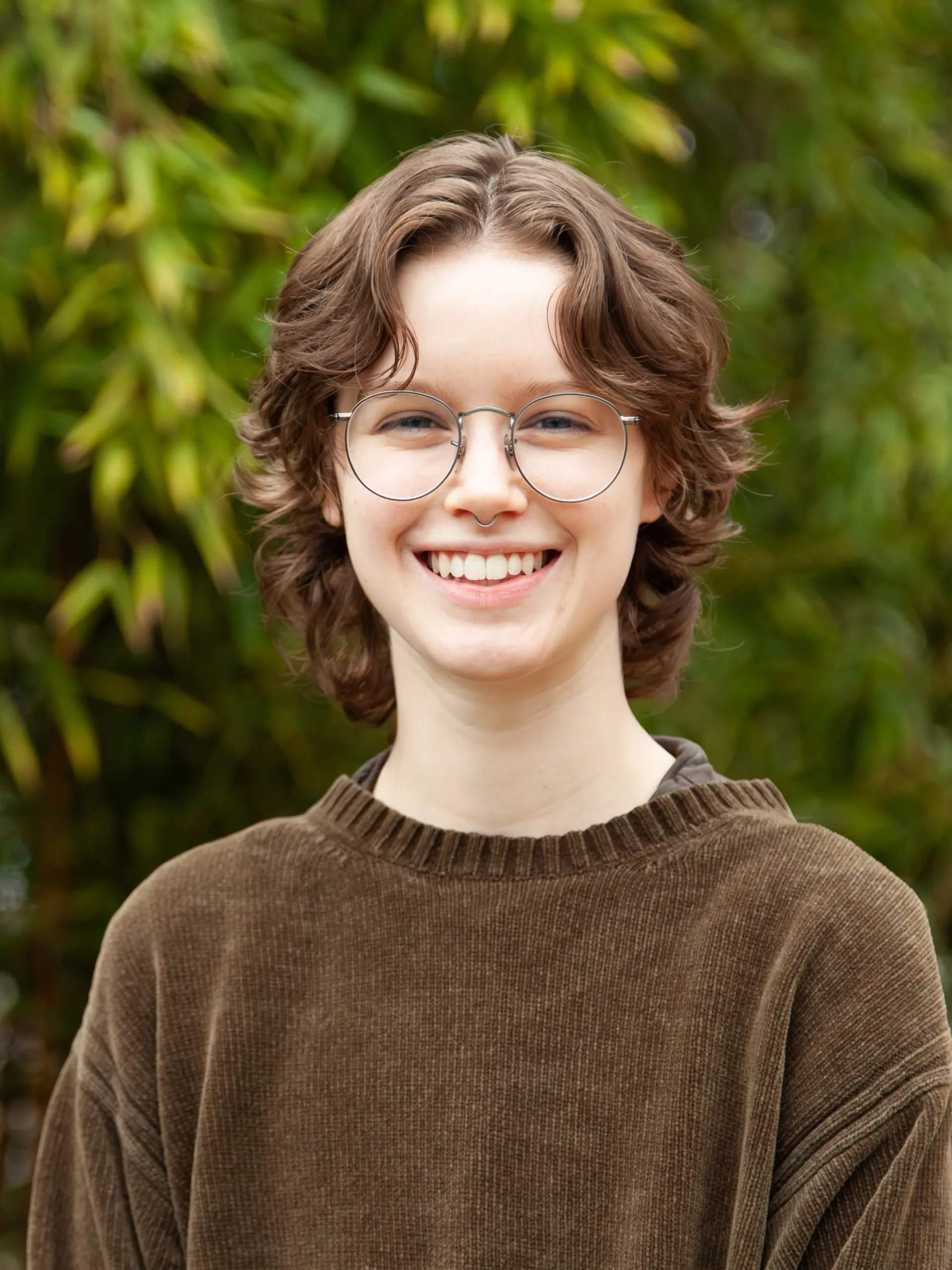 A woman smiling with long dark hair and earrings on.