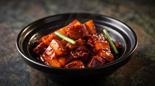 Black bowl of spicy braised meat or tofu cubes garnished with green onion on a dark table