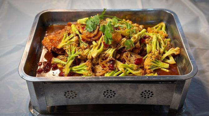Tray of cooked broccoli in sauce garnished with herbs, served in a metal buffet pan