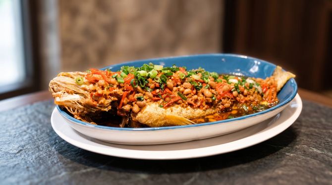 Blue plate of fried fish topped with chopped herbs and sauce on a white plate and dark table