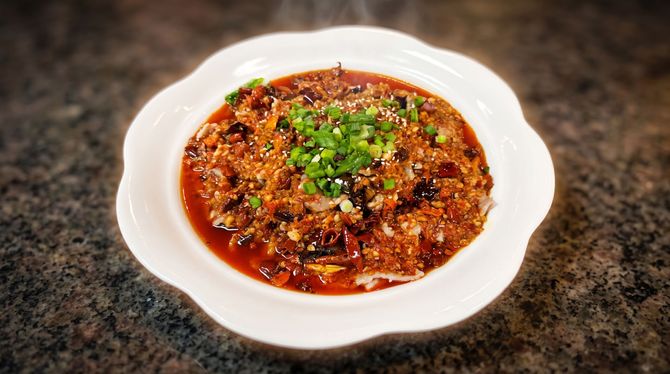 White bowl of spicy red stew topped with chopped herbs on a dark countertop