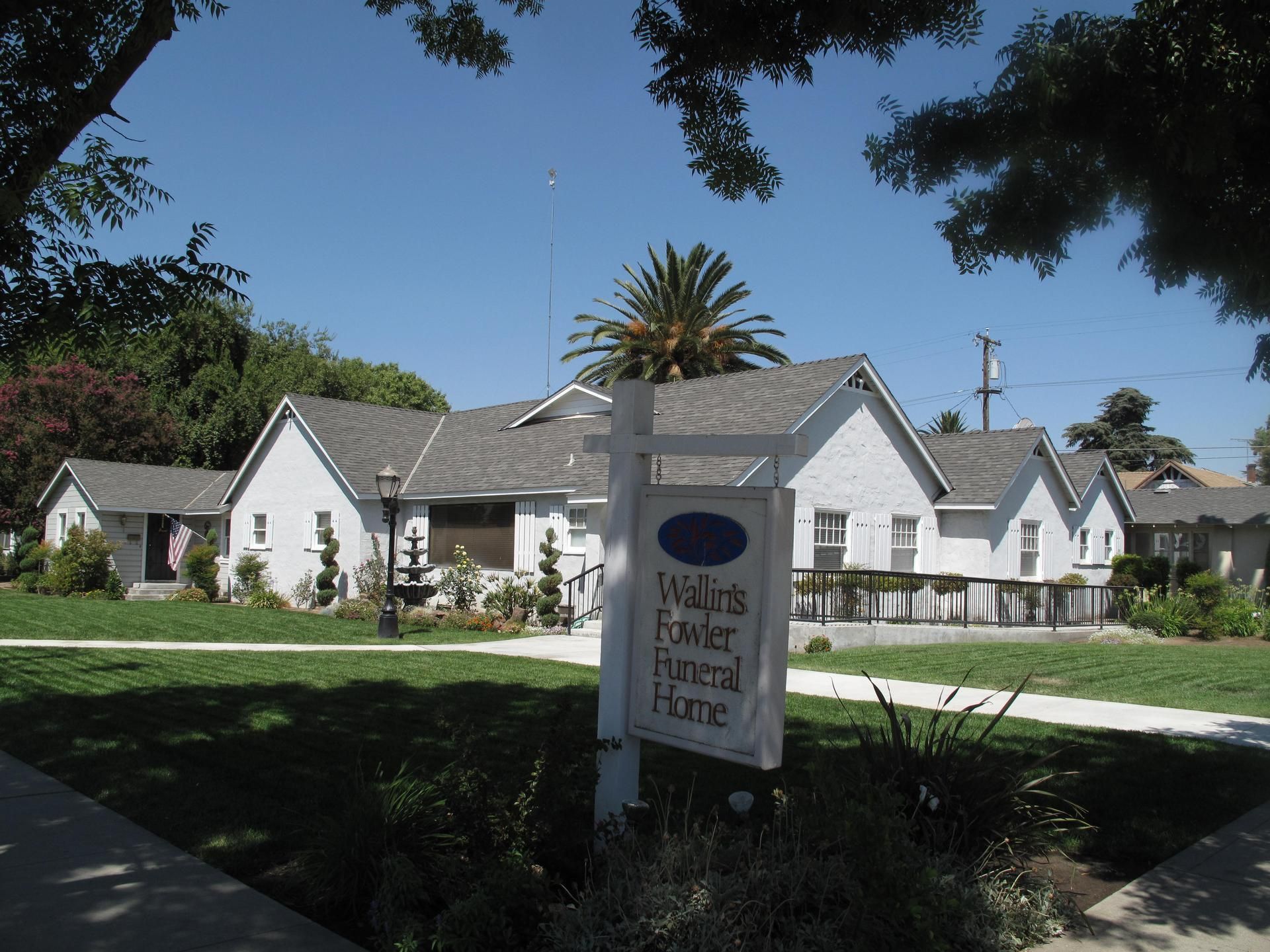 White cottages with gray roofs behind a sign, viewed from a shaded grassy lawn under a blue sky