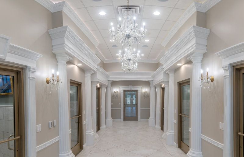 A long hallway with columns and a chandelier hanging from the ceiling.
