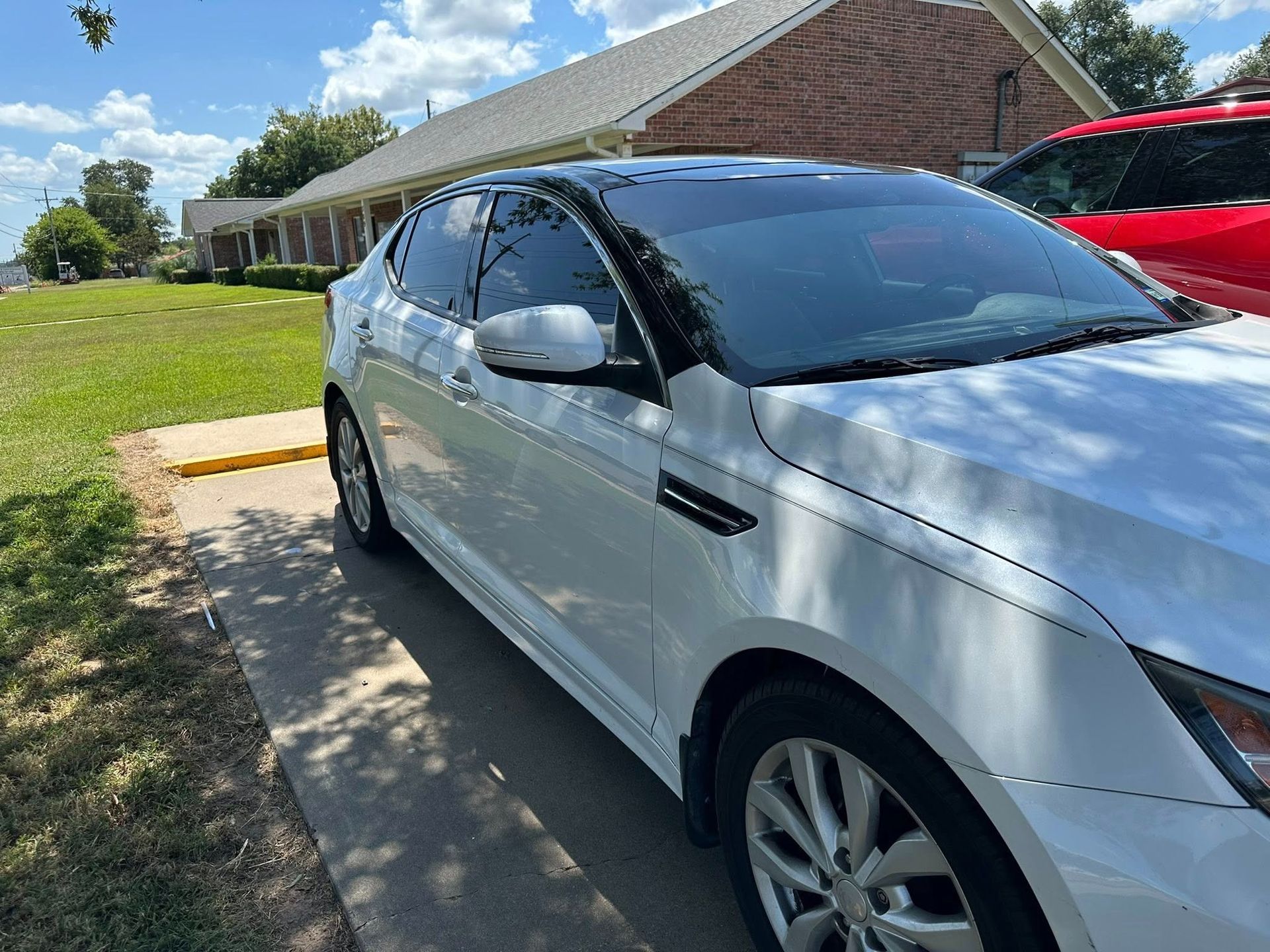 White sedan parked in a driveway beside a house on a sunny day