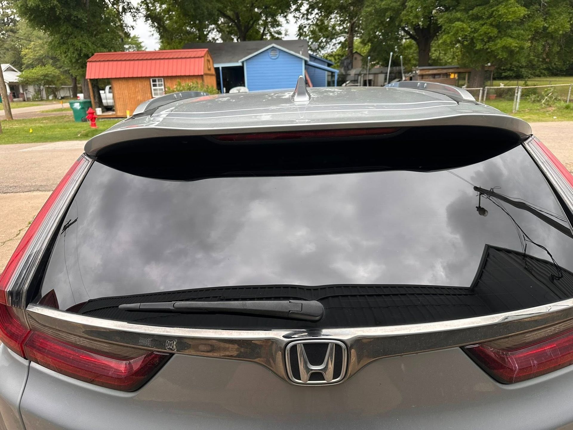 Rear view of a red Honda with a shattered rear window and a cracked windshield in a parking lot.