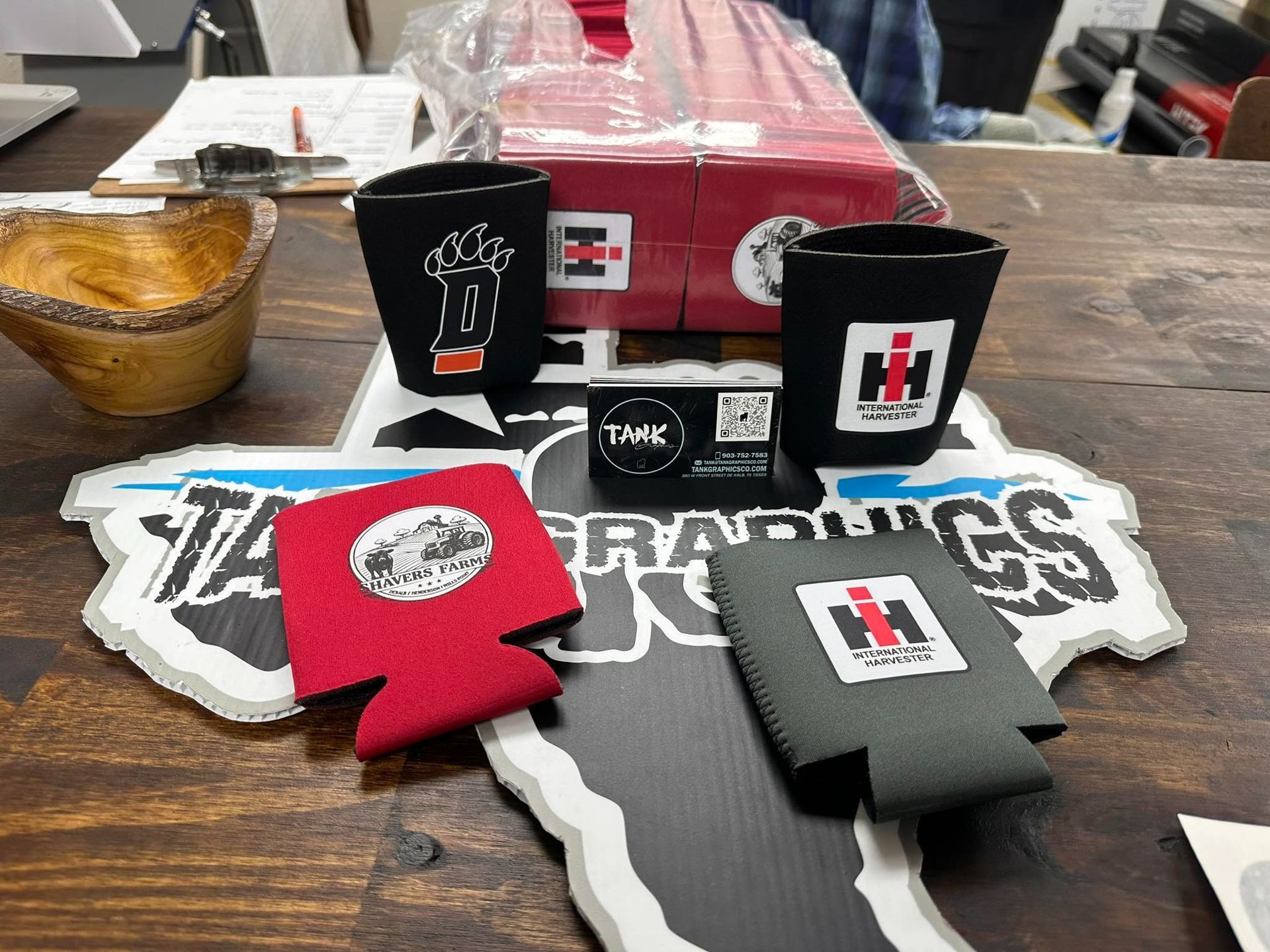 Black and red koozies and cups displayed on a table with branded logos and a box in the background