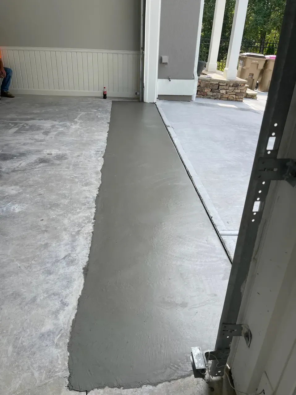 A patch of new, smooth gray concrete fills a section of an otherwise weathered concrete garage floor.