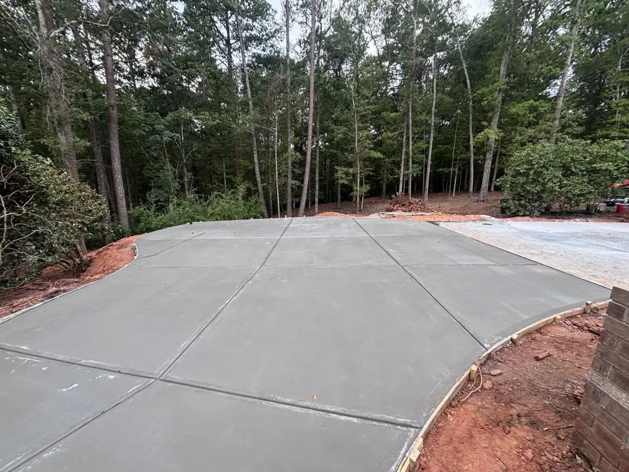 A newly poured concrete driveway apron transitions into a gravel driveway in a wooded residential setting.