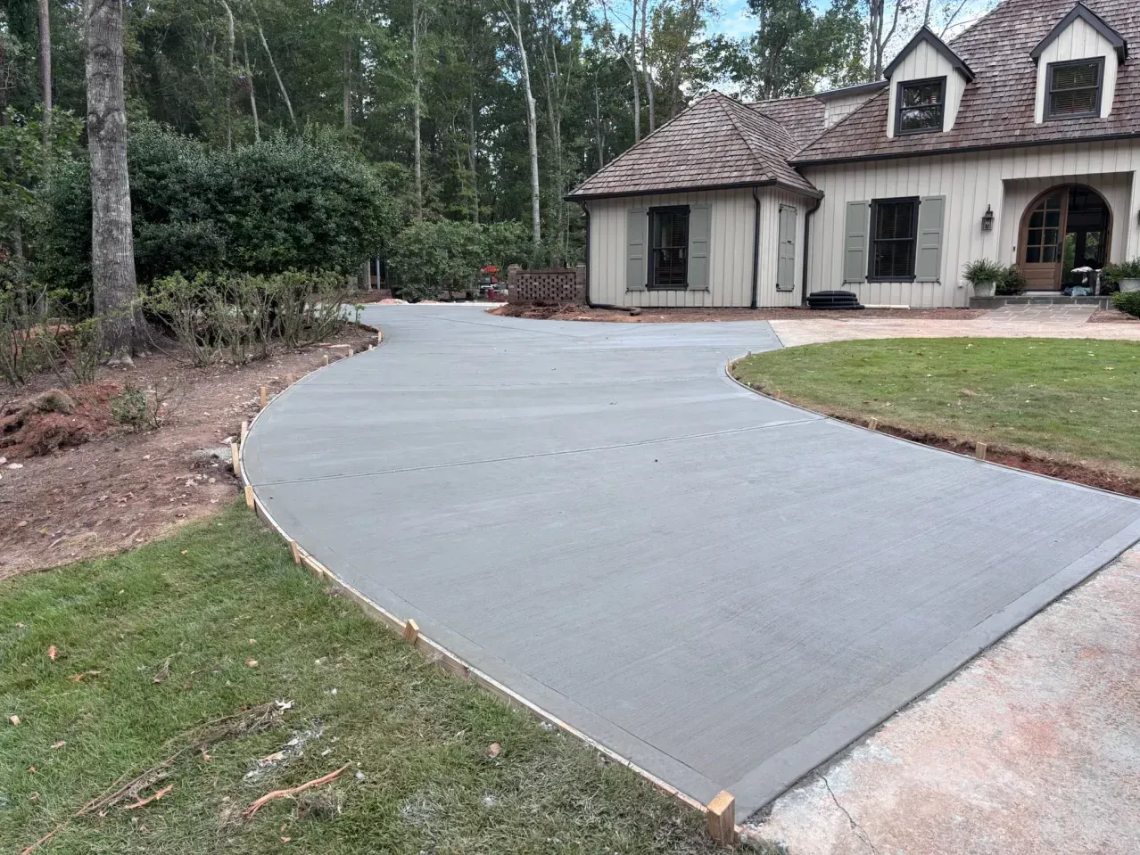 A freshly poured, smooth gray concrete driveway leads up to the front entrance of a two-story home with a tiled roof.