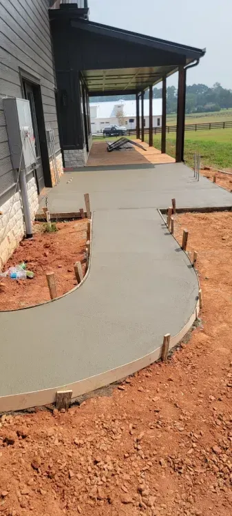 Freshly poured concrete patio and curved walkway with wooden forms still in place next to a house under construction.