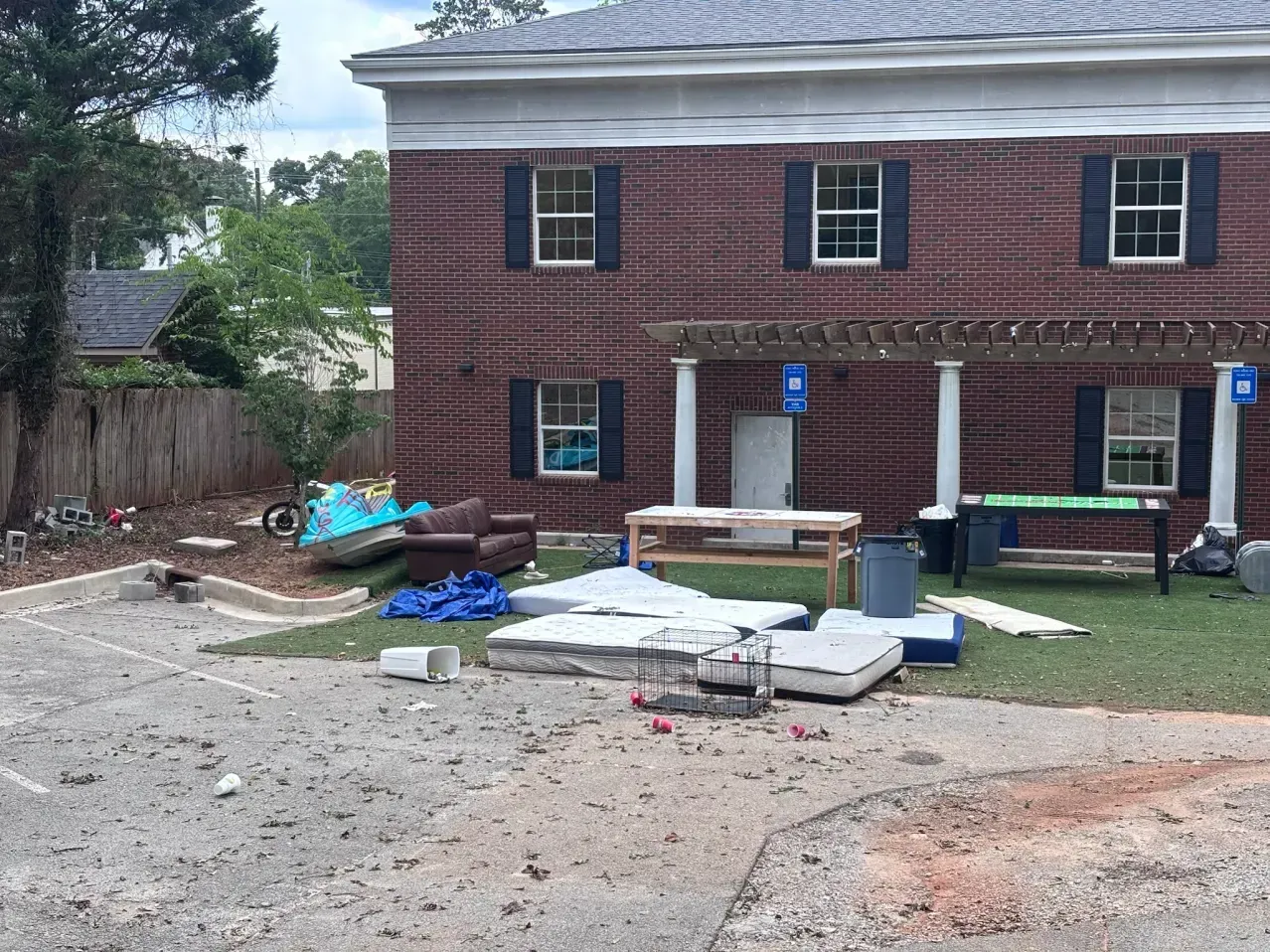 Discarded furniture, including mattresses and a couch, sits in front of a red brick building with a white porch.