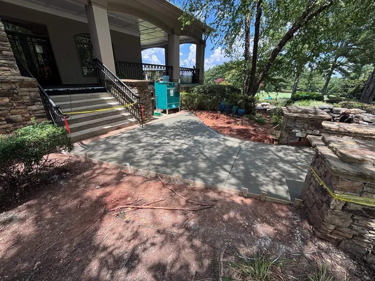 A new concrete walkway leads to stone stairs at the entrance of a house, marked off by yellow caution tape.