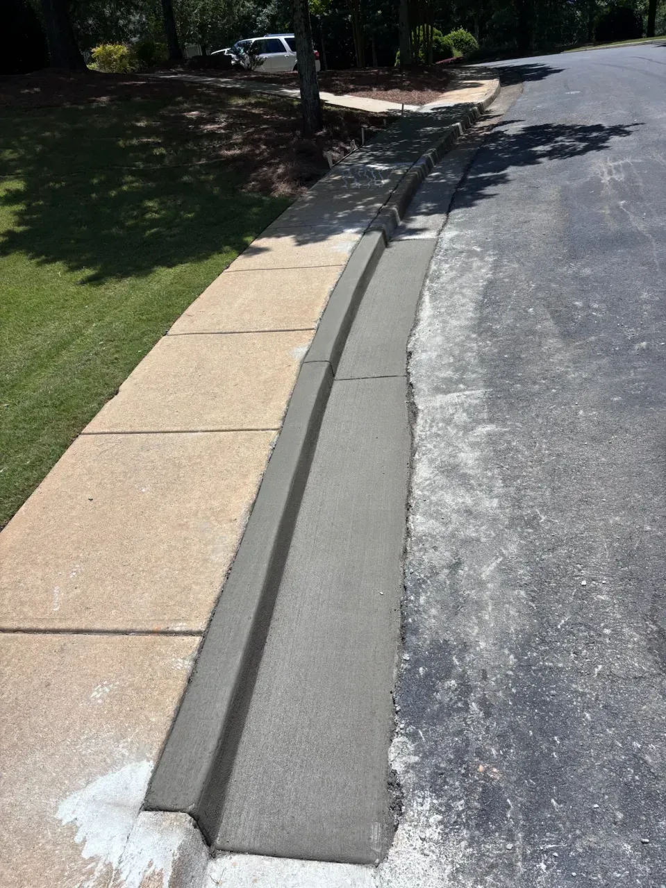 A fresh concrete curb ramp installed between a sidewalk and an asphalt road.