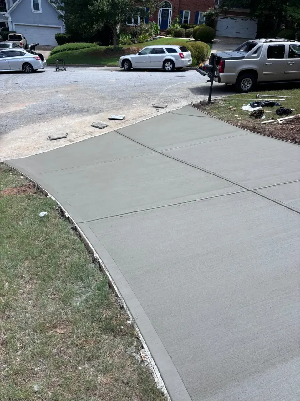 A newly poured concrete driveway apron transitions from a gravel road to a residential driveway in a suburban neighborhood.
