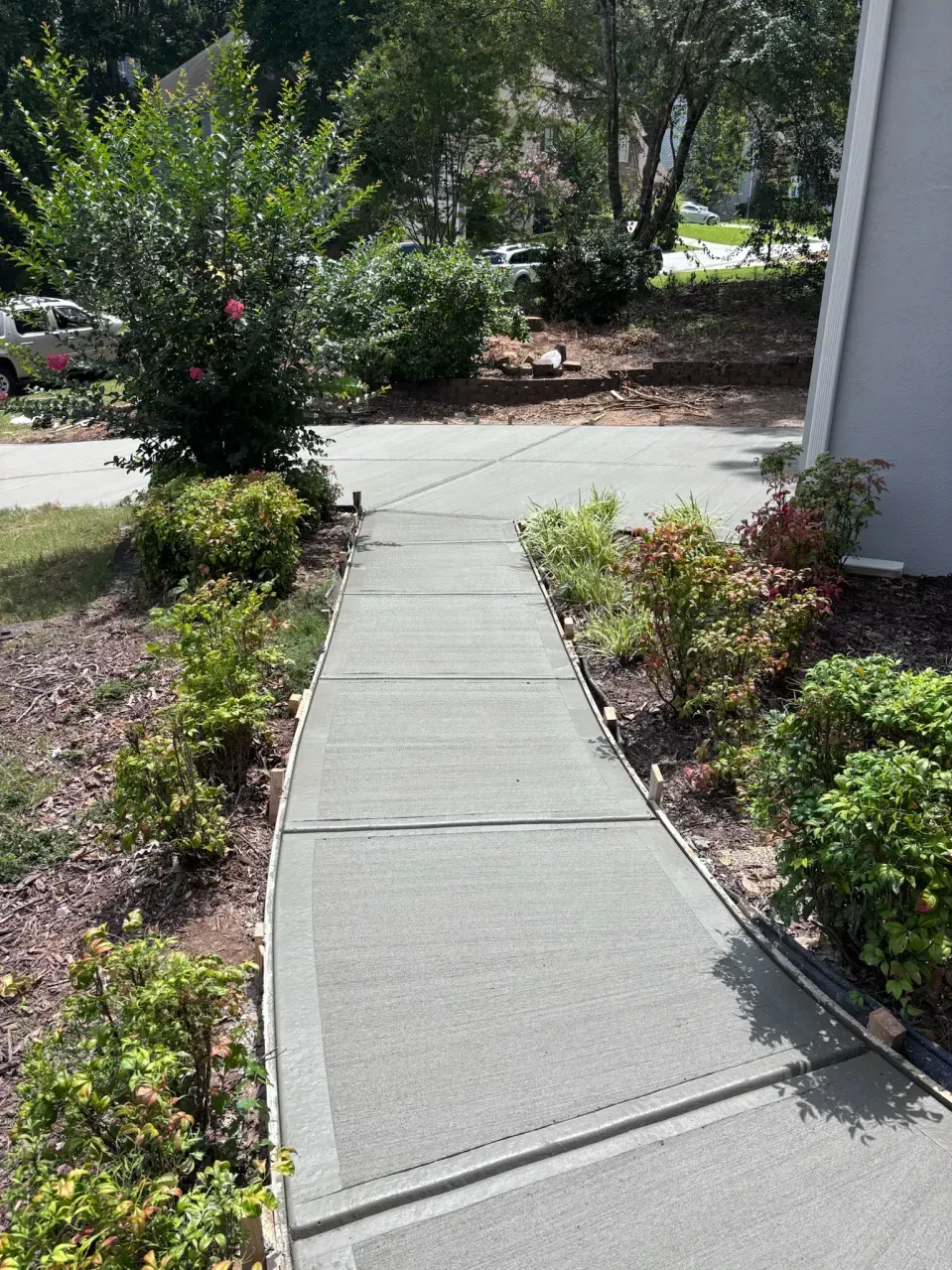 A straight, paved walkway leads outdoors, bordered by landscaping with small shrubs and mulch on either side.