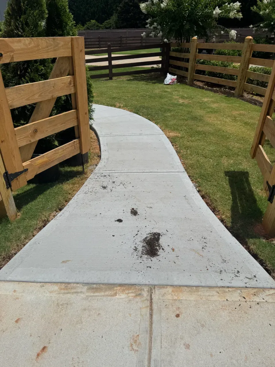 A curving concrete sidewalk path leading between two wooden fences onto a grassy lawn.