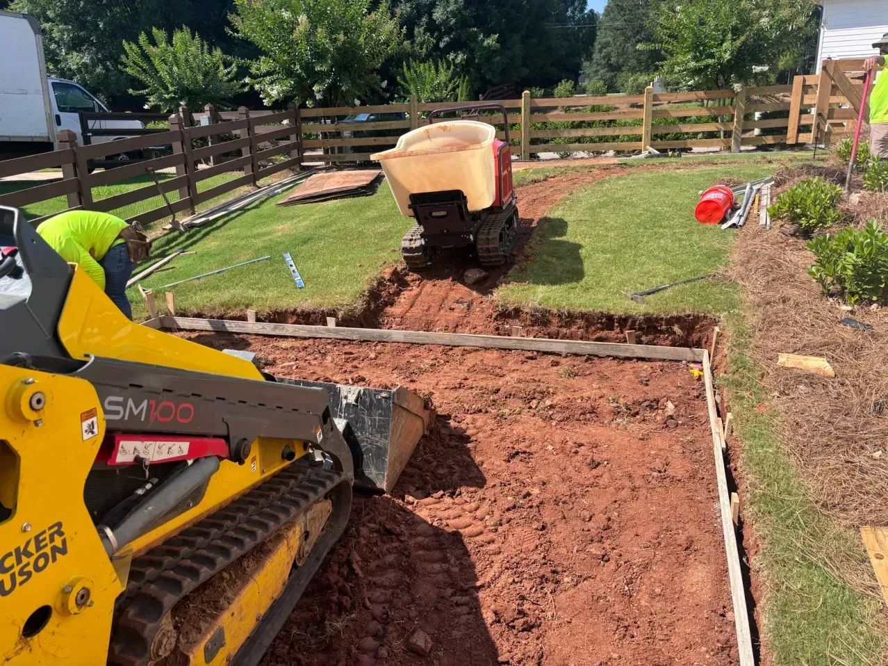 A yellow skid steer loader and a small track dumper on a construction site excavating dirt for a new walkway.