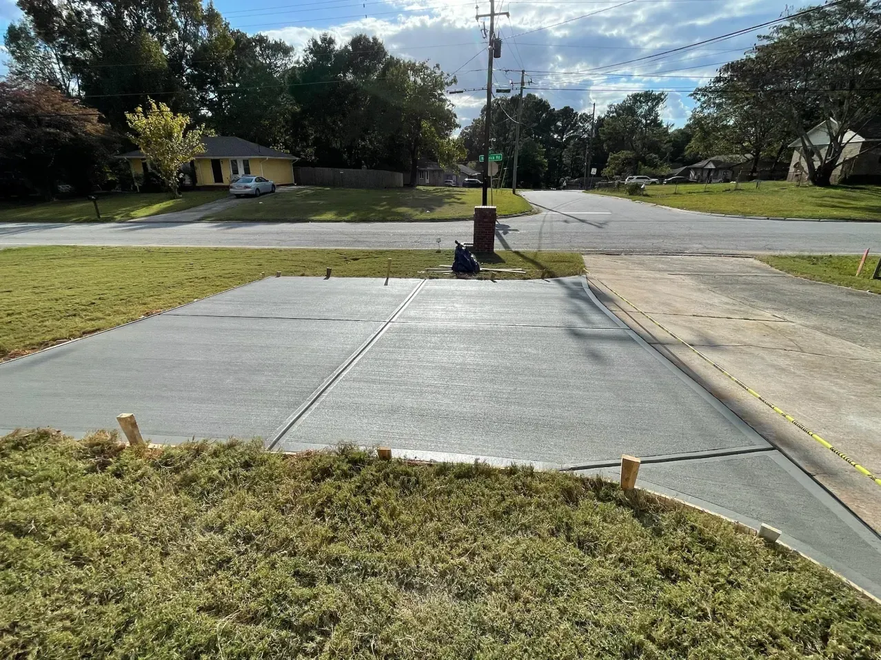 A freshly poured rectangular concrete driveway pad sits in a grassy front yard next to an existing concrete driveway.