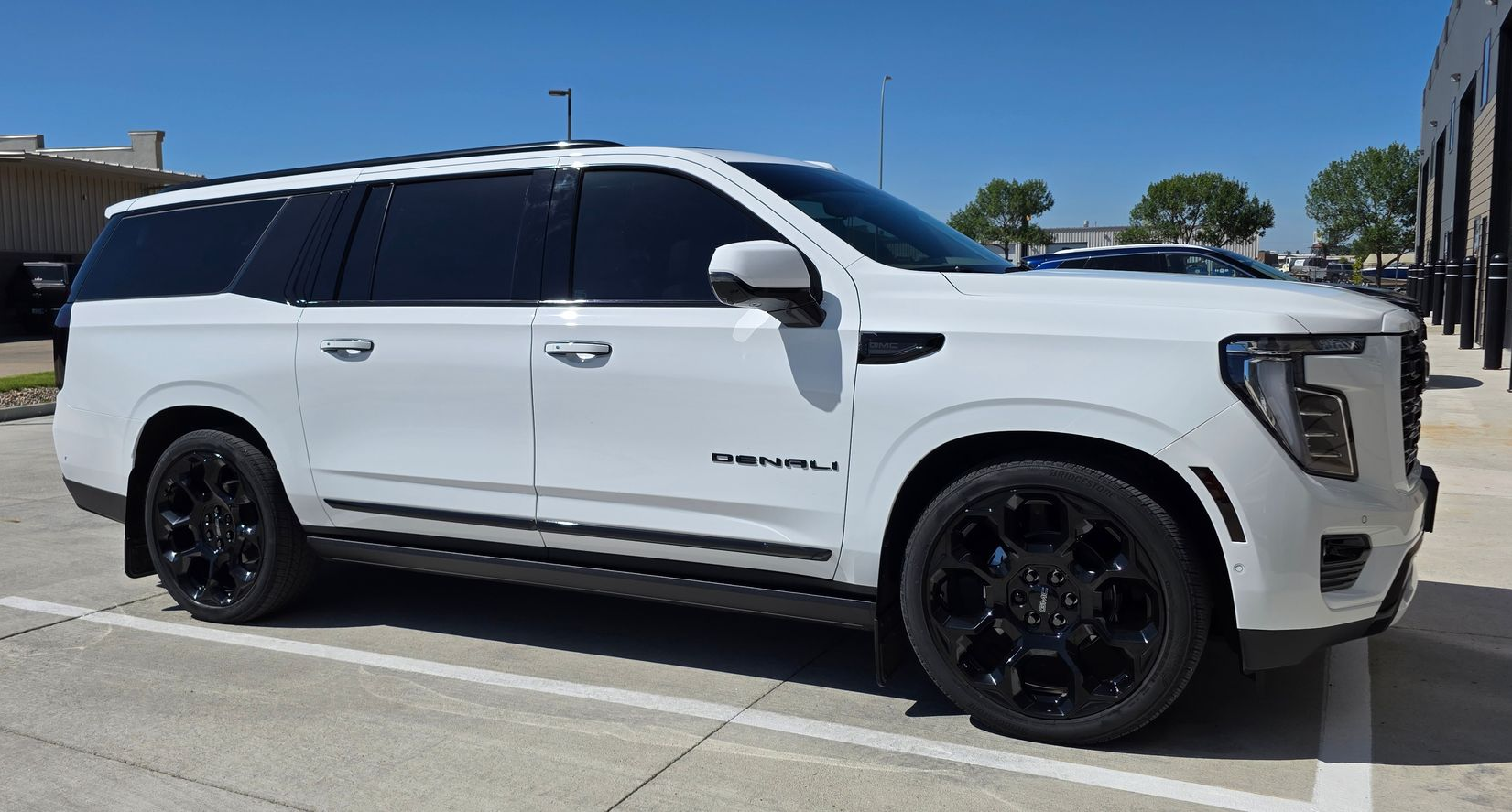 White GMC Yukon Denali SUV with black wheels parked outside on a sunny day.
