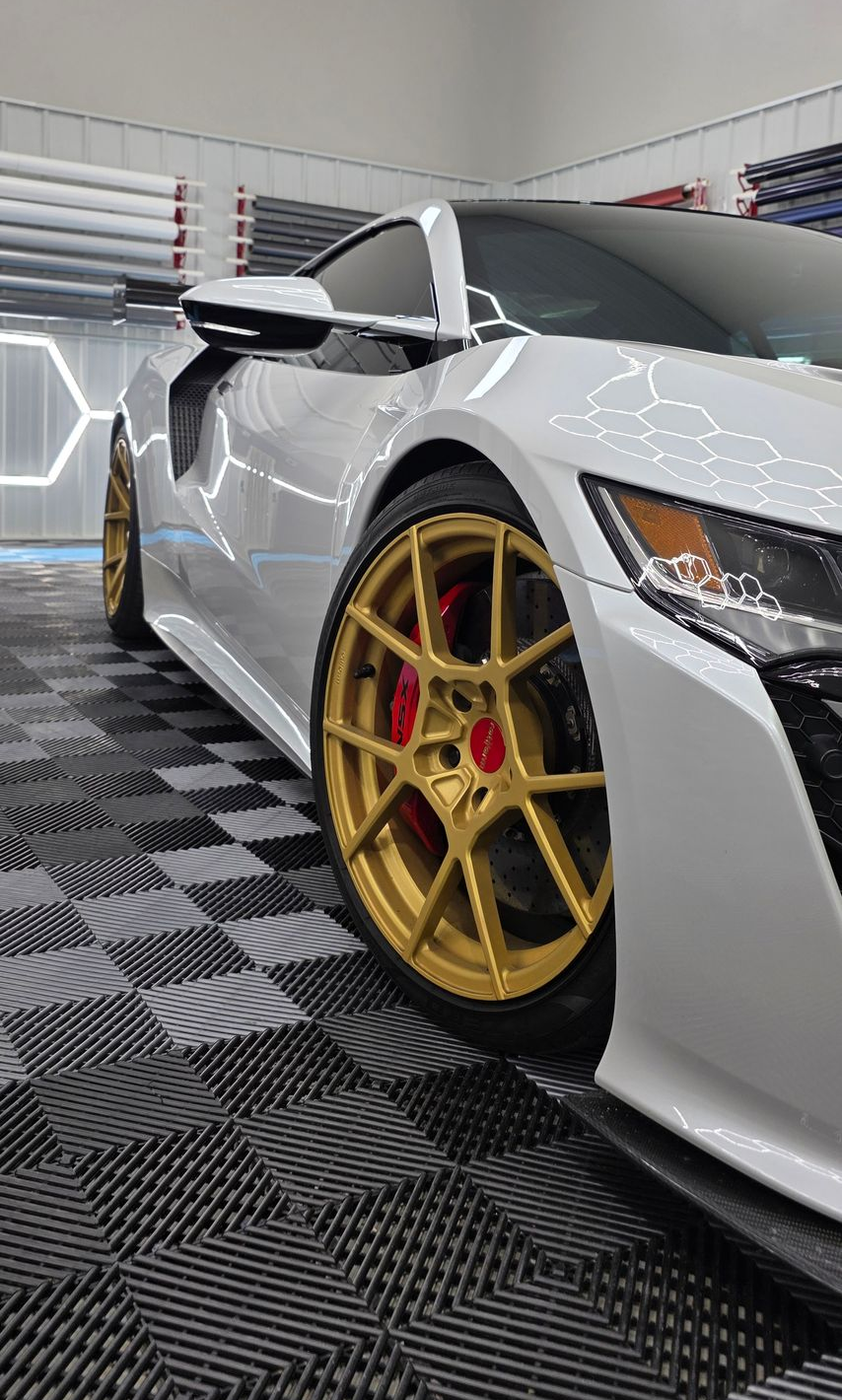 White sports car with gold wheels, red calipers, parked on checkered floor.