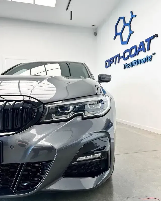 Gray sports sedan in a bright auto detailing shop with Opti-Coat Protection logo on the wall