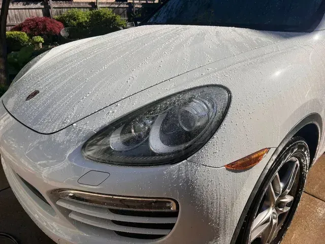 White sports car front end covered in water droplets, parked outdoors in sunlight