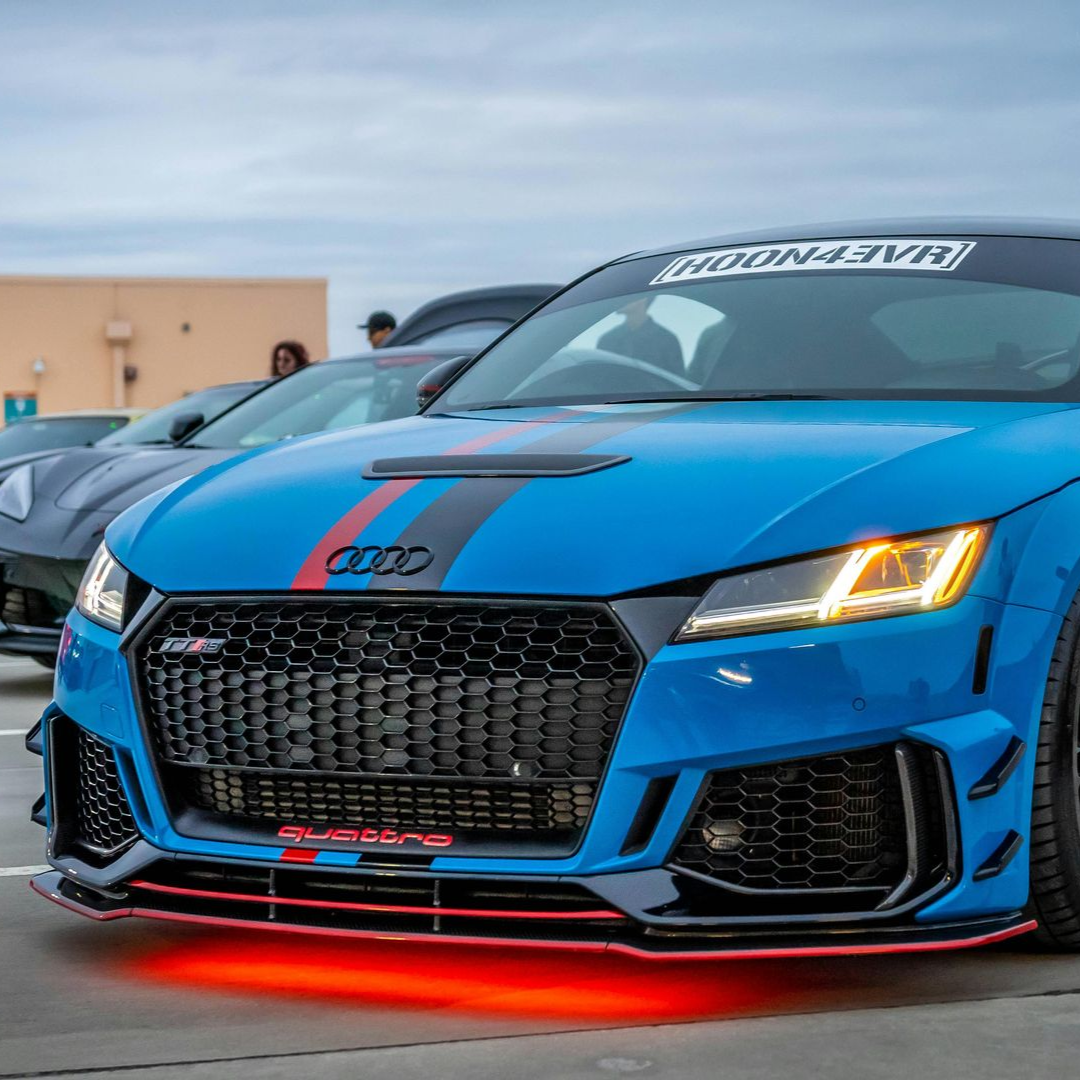 Blue Audi TT modified with red accents and illuminated underglow. Parked outdoors.