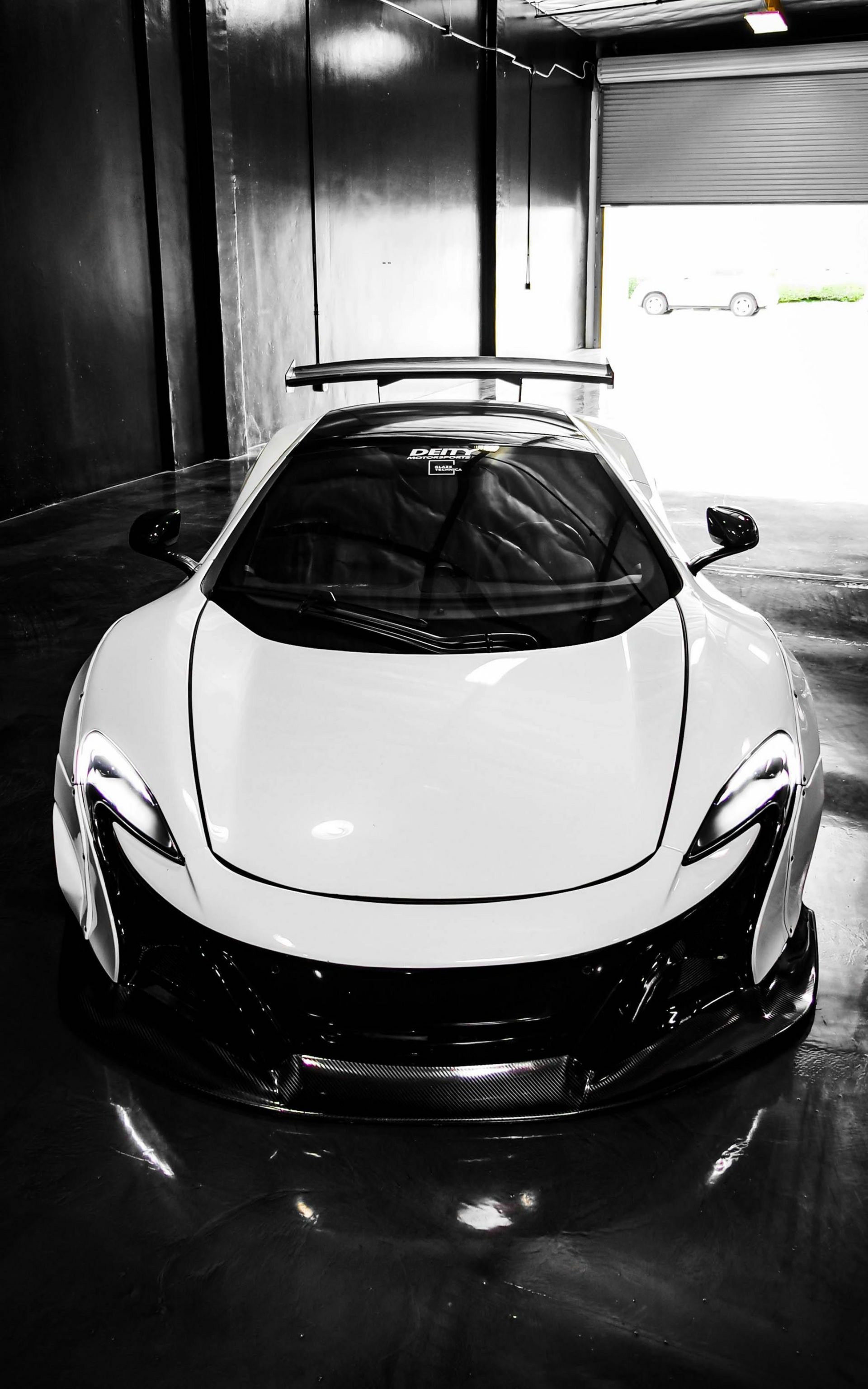 White McLaren sports car in a garage with headlights on and a rear spoiler.