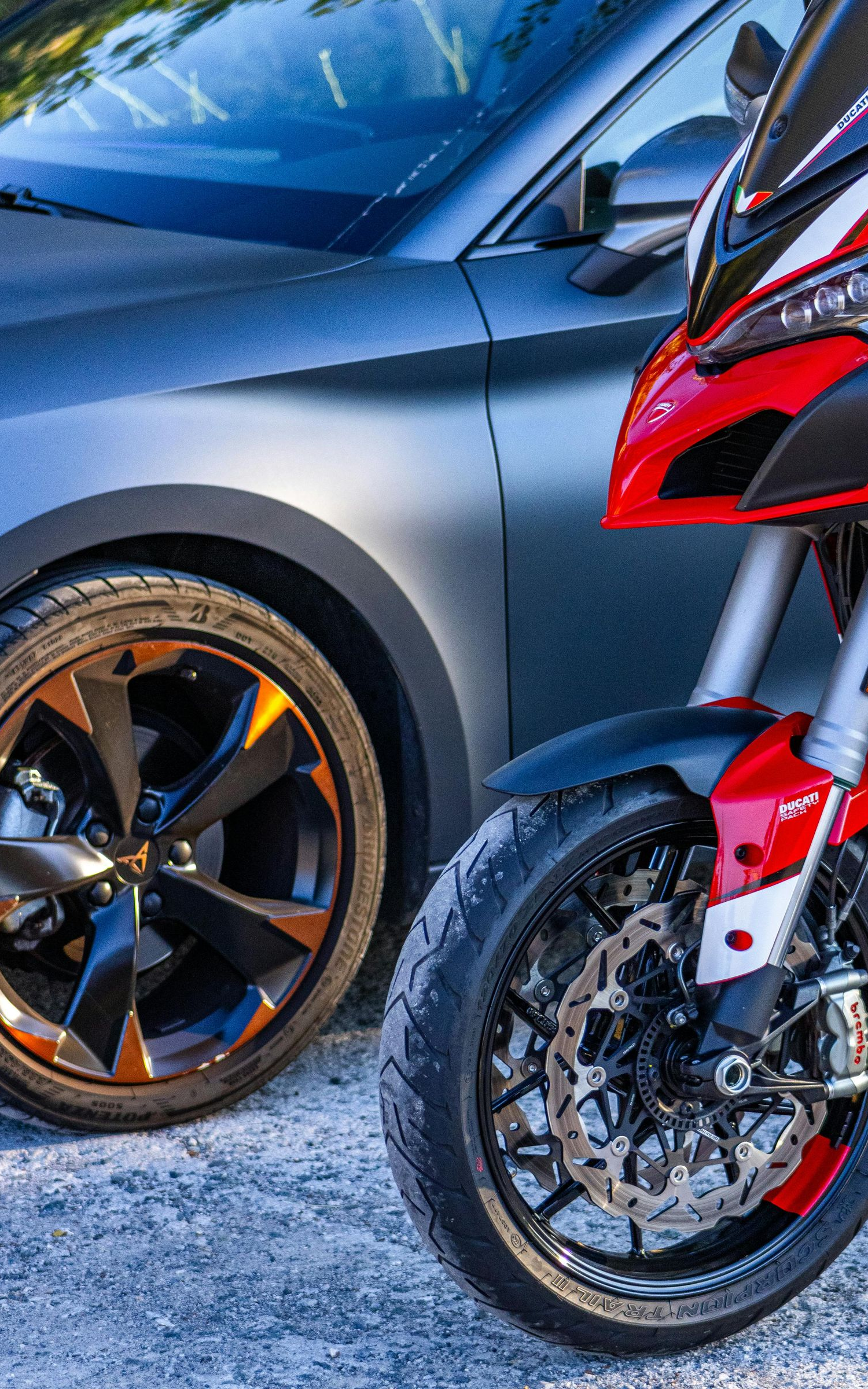 Gray car and red motorcycle parked side-by-side on pavement; close-up of wheels and front of vehicles.