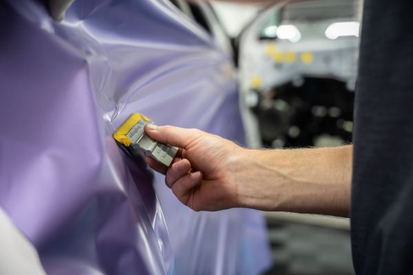 A person is cleaning a blue car with an orange towel
