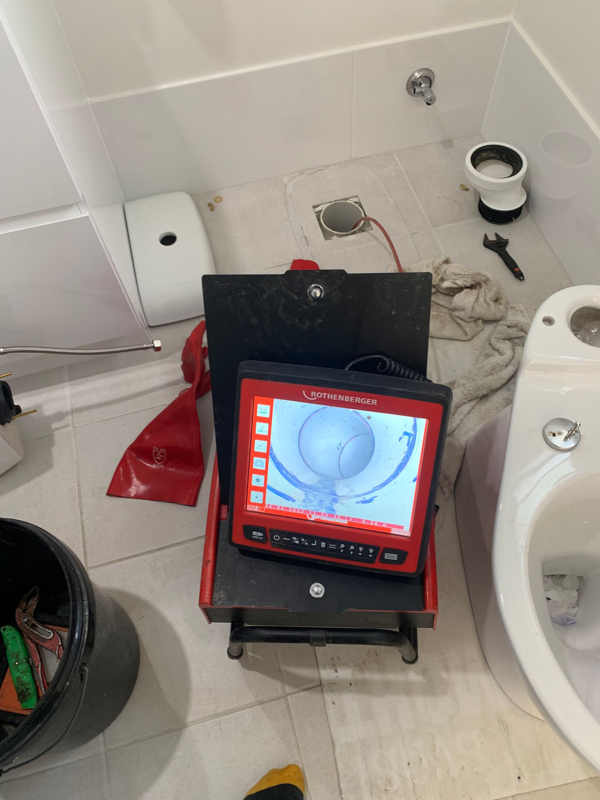 A plumbing camera set up to find blockage issues going down a pipe and some tools around on a tiled floor — Delaney Plumbing Services In Taree, NSW