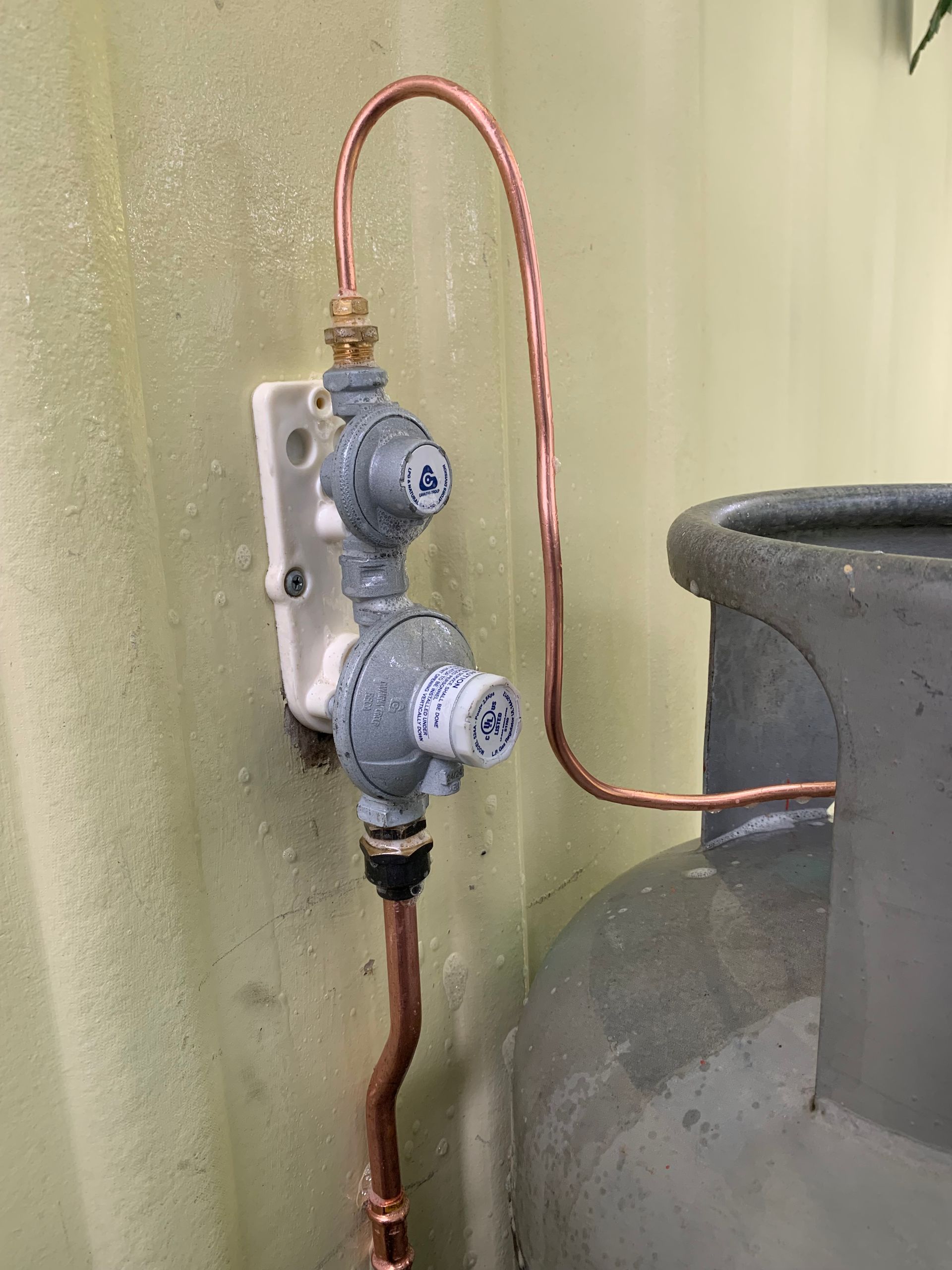A close up of a gas bottle with copper hoses and the pressure valves connected to a wall — Delaney Plumbing Services In Taree, NSW
