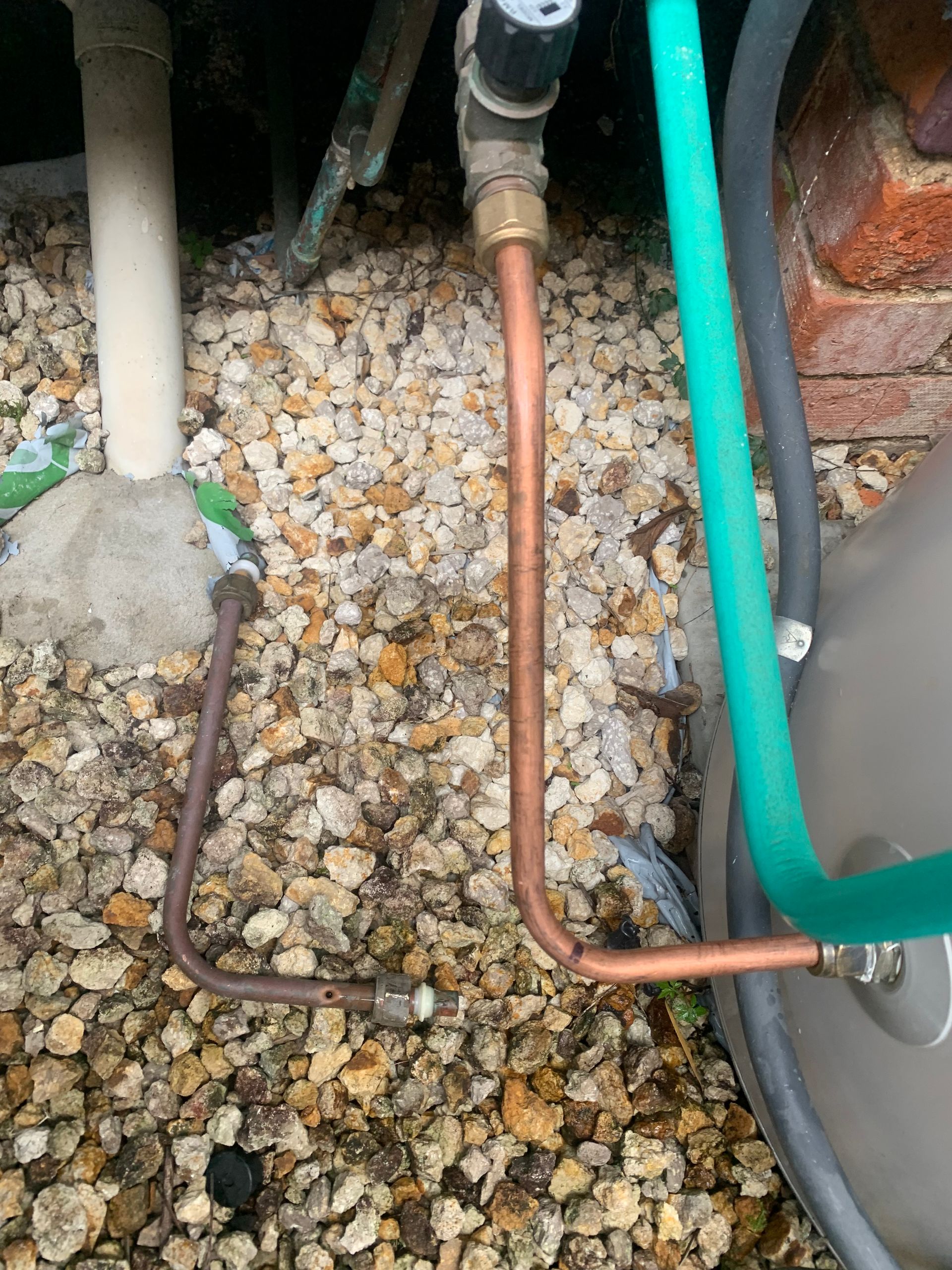 A close up of gas pipes coming out of a cylinder on some gravel — Delaney Plumbing Services In Old Bar, NSW